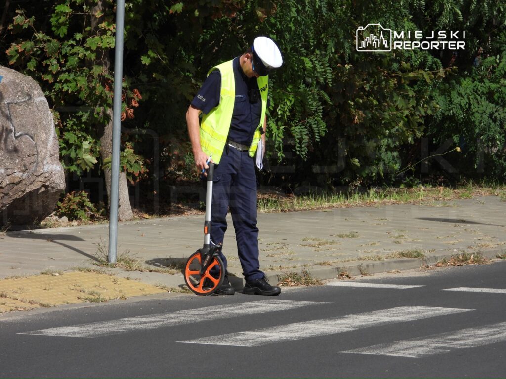 Policjant w odblaskowej kamizelce mierzy długość przejścia dla pieszych przy ulicy, korzystając z dalmierza.