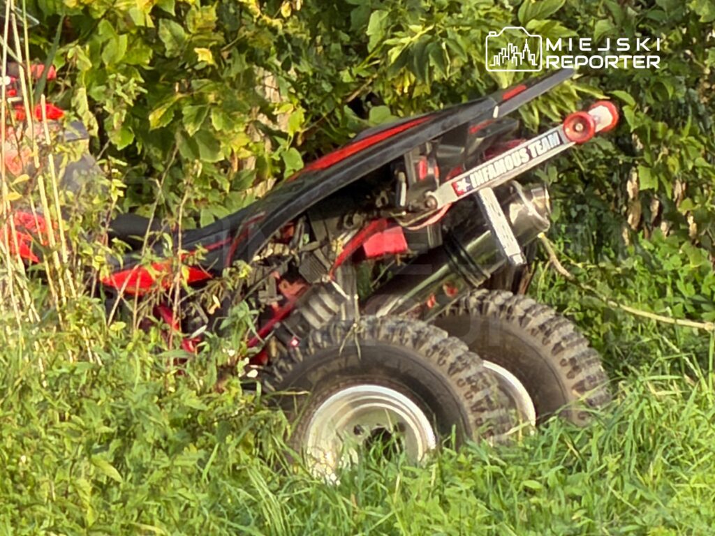 Czerwony quad ukryty w gęstej zieleni, z widocznymi dużymi oponami i elementami silnika.