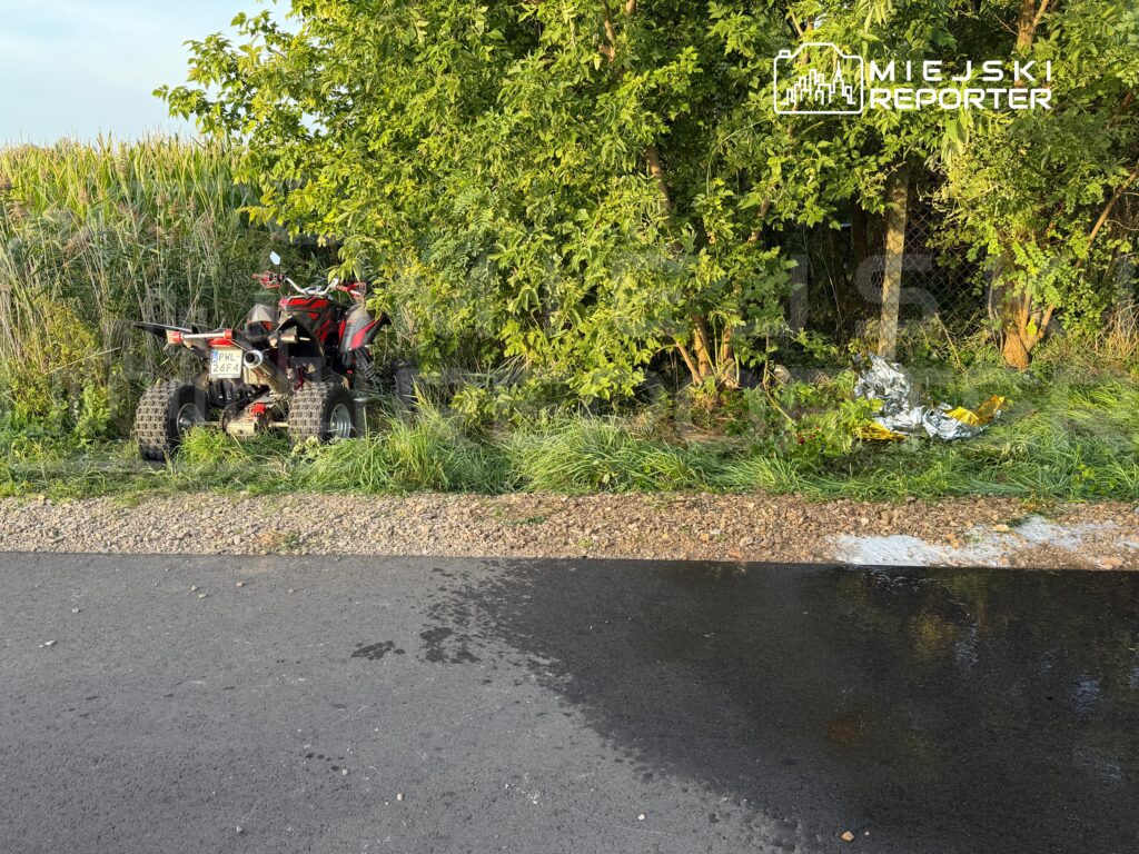 Czarny quad zaparkowany obok gęstych krzewów na poboczu drogi, w tle widoczne fragmenty folii.