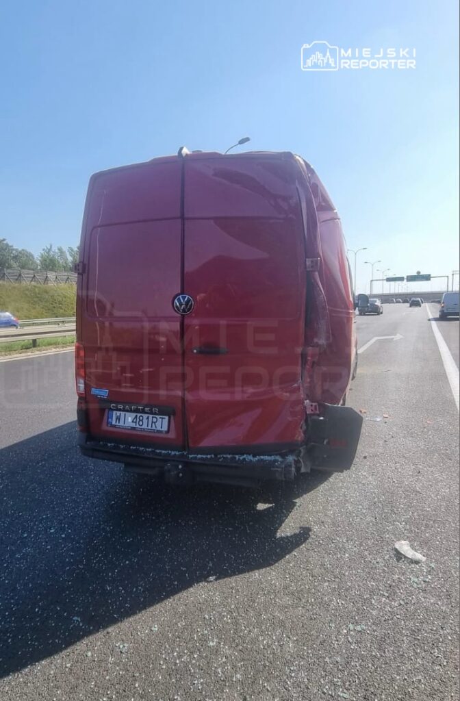 Czerwony furgon z uszkodzoną tylną częścią stoi na pasie ruchu, obok widać fragmenty szkła na nawierzchni.