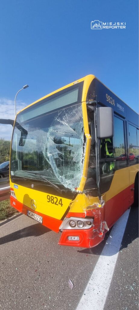 Uszkodzony autobus z pękniętą szybą i wgnieceniem na przodzie stoi na drodze.