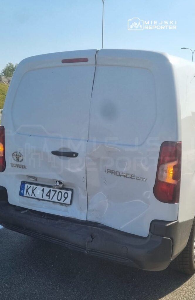 Biały furgon marki Toyota z widocznymi uszkodzeniami tyłu, zaparkowany na drodze.