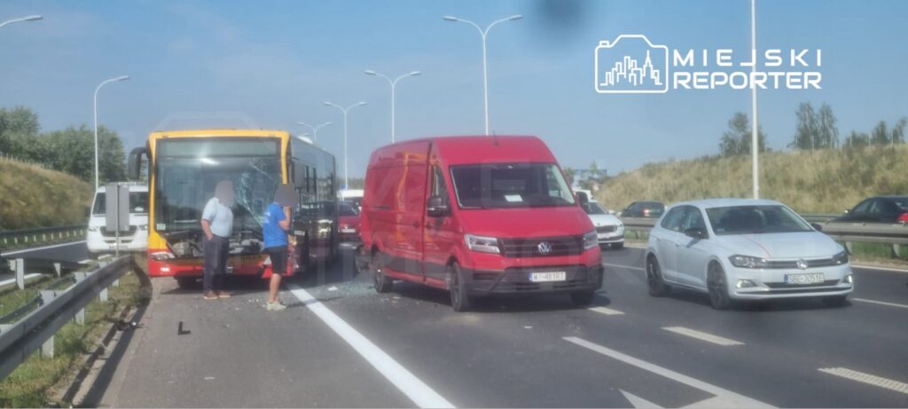 Na drodze doszło do wypadku, w którym autobus z uszkodzoną szybą stoi obok czerwonego samochodu dostawczego, a kierowcy rozmawiają.