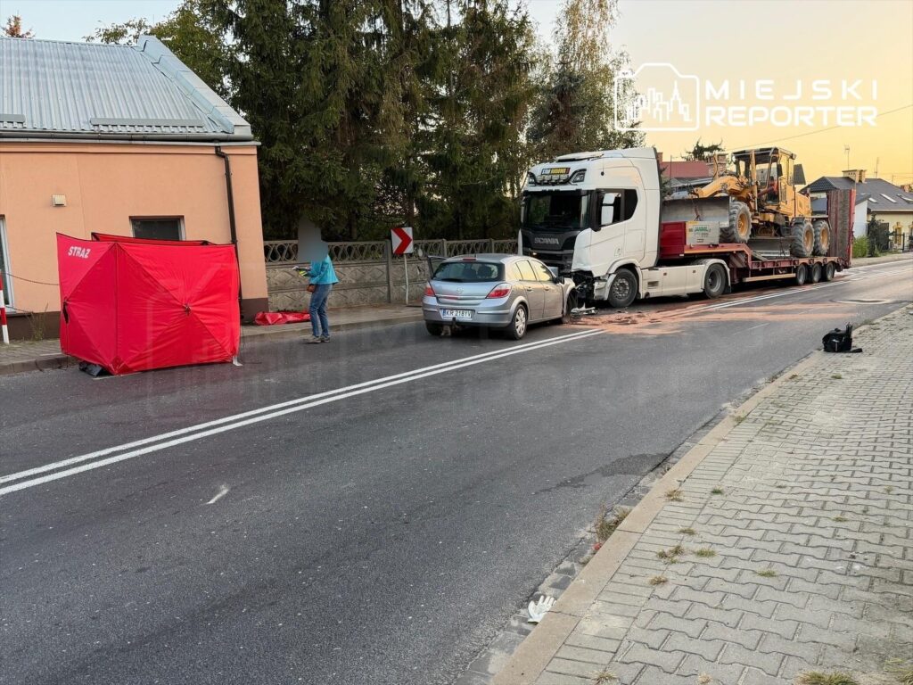 W miejscu wypadku na drodze, strażacy zabezpieczają teren, a ciężarówka z przyczepą stoi obok uszkodzonego osobowego auta.