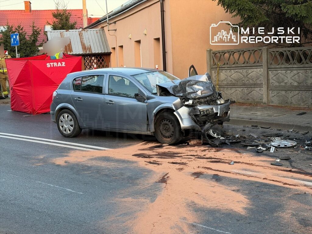 Zniszczony samochód osobowy leży na drodze, obok rozstawiony czerwony namiot straży pożarnej oraz ślady na jezdni.