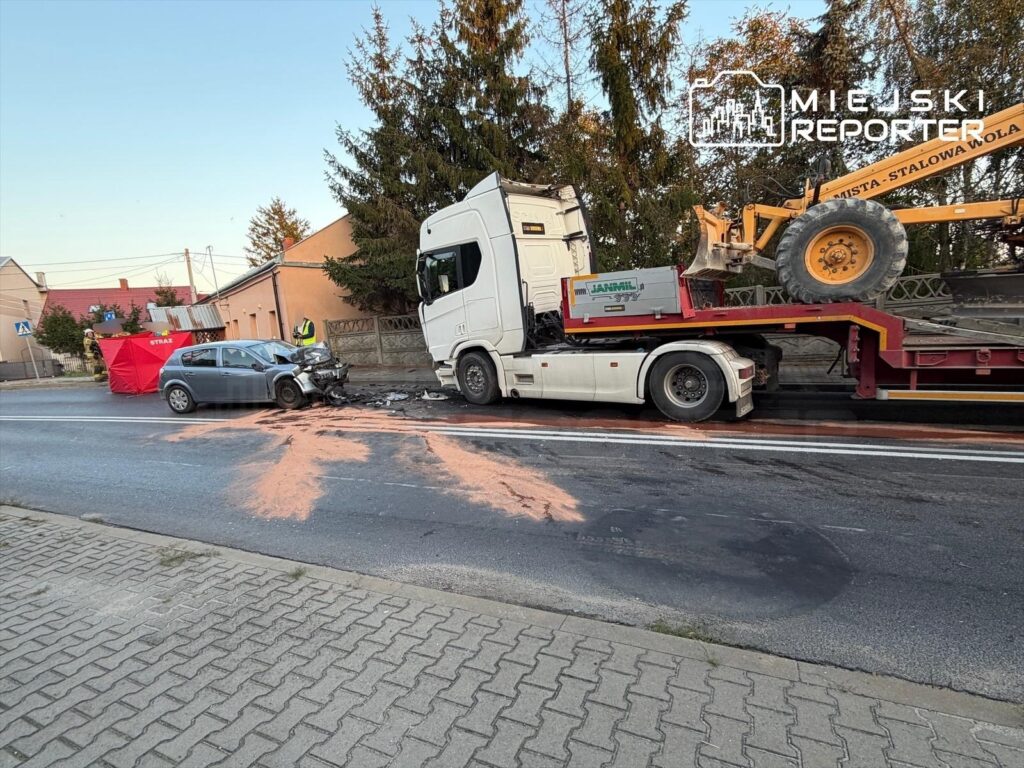 Wypadek drogowy z udziałem osobowego auta i ciężarówki, na jezdni widoczne uszkodzenia oraz rozsypany materiał.