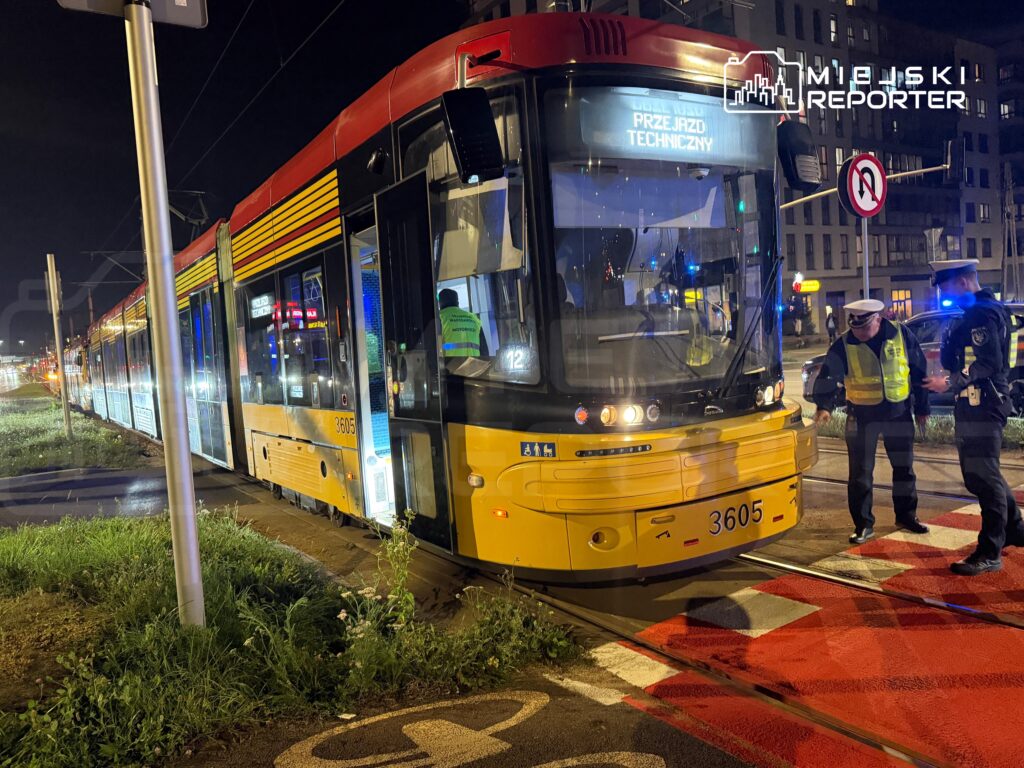 Tramwaj nocny zatrzymany na torowisku, obok którego rozmawia dwóch policjantów w kamizelkach odblaskowych.
