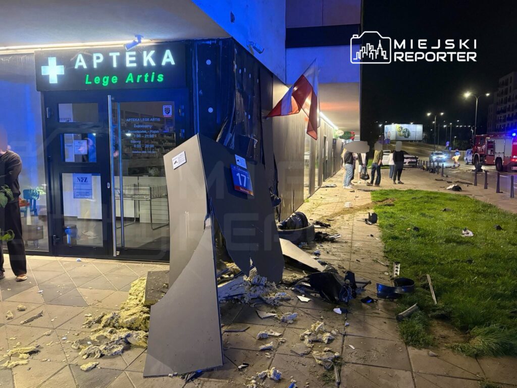 Zniszczona elewacja apteki z neonowym napisem „APTEKA Lege Artis” oraz rozbite fragmenty otoczenia, w nocy.