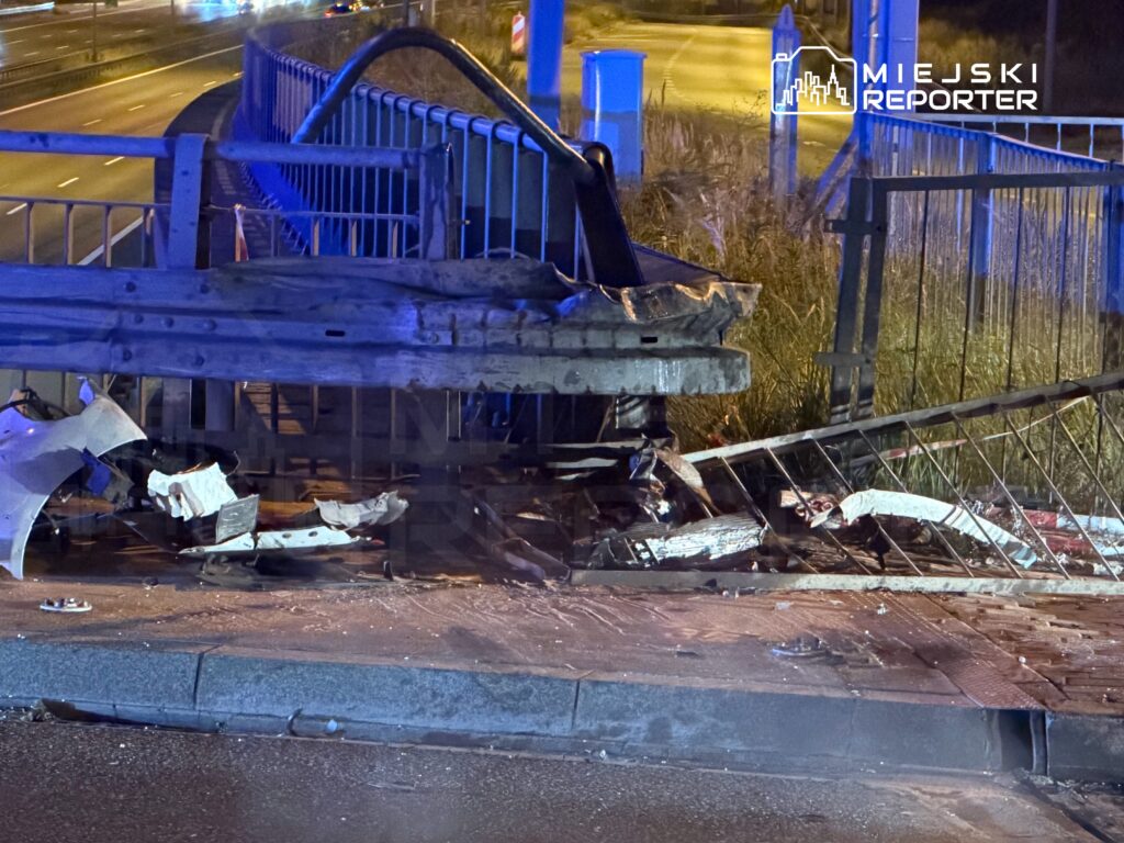 Zniszczony fragment bariery ochronnej na moście, obok uszkodzone resztki pojazdu na poboczu drogi.