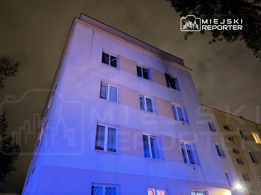 Nowoczesny budynek mieszkalny z oświetleniem nocnym, widoczny z perspektywy dolnej, z chmurami na niebie.