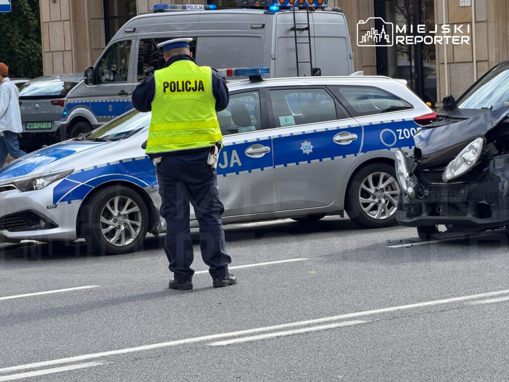 Policjant w kamizelce odblaskowej bada miejsce wypadku drogowego z udziałem dwóch pojazdów.