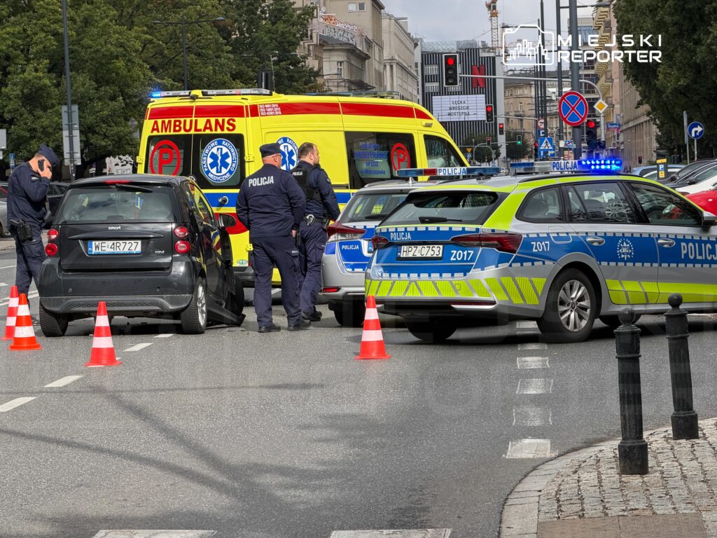 Na jezdni zatrzymane są dwa radiowozy policyjne oraz karetka pogotowia, obok stoi czterech policjantów.