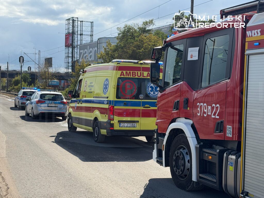 Ambulans i wóz strażacki zatrzymane na drodze, obok policyjny radiowóz z włączonymi sygnałami świetlnymi.