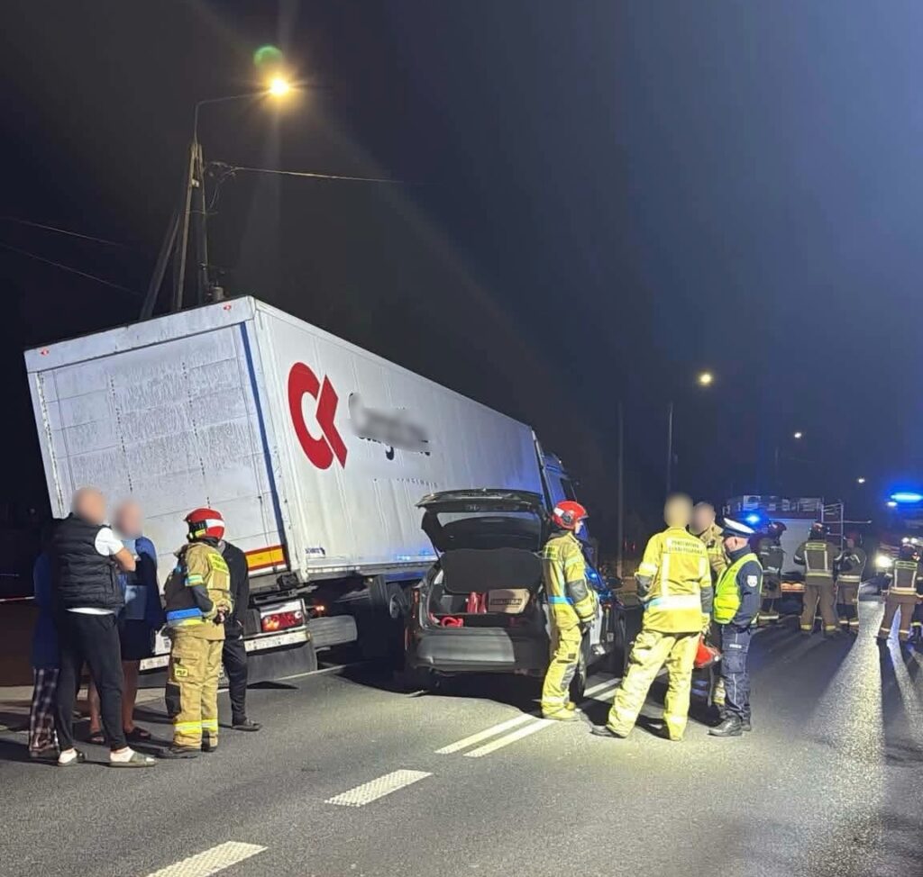 Grupa ratowników i policjantów udziela pomocy poszkodowanym przy przewróconej ciężarówce na drodze nocą.