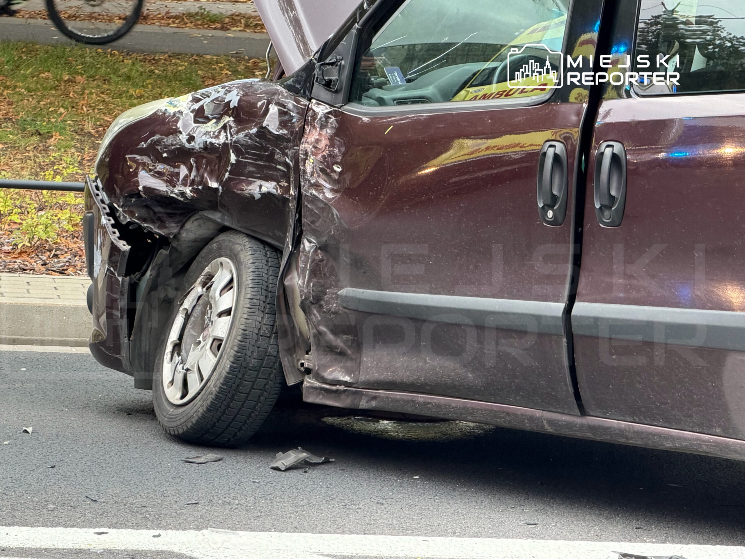 Uszkodzony samochód dostawczy z wgniecioną boczną częścią stoi na jezdni, obok widoczny rowerzysta.