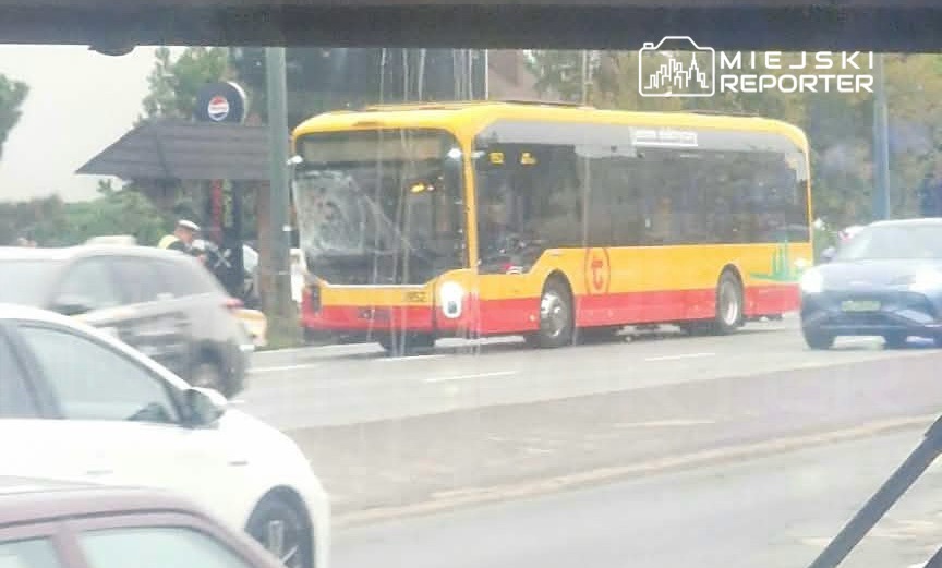 Autobus komunikacji miejskiej zatrzymany na przystanku, obok przejeżdżające samochody w deszczowej aurze.