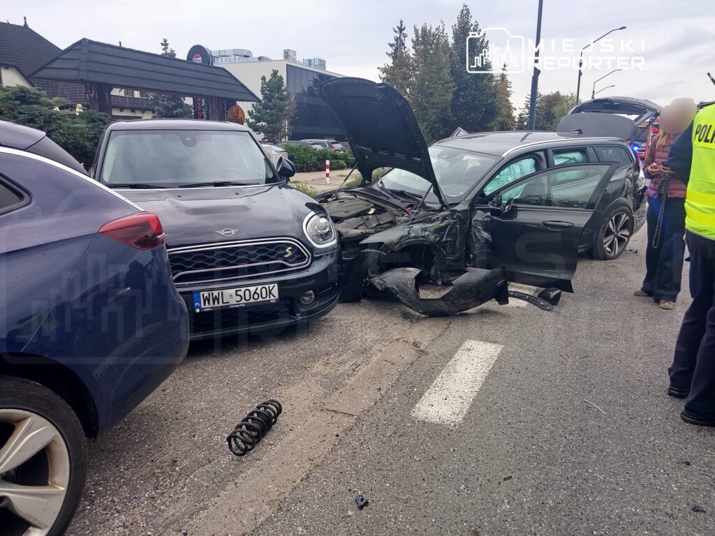 Wielokrotny zderzenie dwóch samochodów osobowych na drodze, z widocznymi uszkodzeniami pojazdów i osobami w pobliżu.