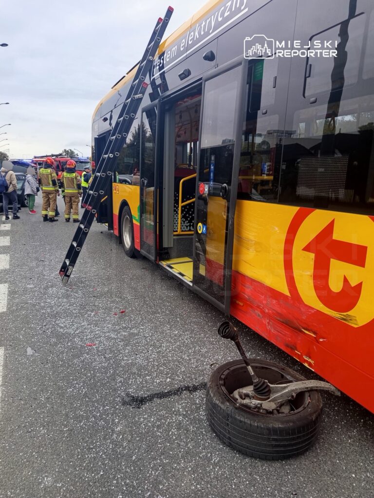 Elektryczny autobus z uszkodzeniami stoi na drodze, obok pracują strażacy, a na jezdni leży odłączone koło.