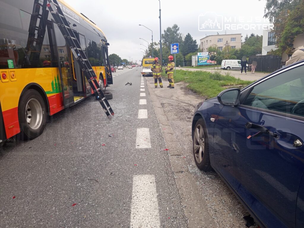Zespół strażaków prowadzi działania ratunkowe obok uszkodzonego autobusu i osobowego samochodu na drodze.