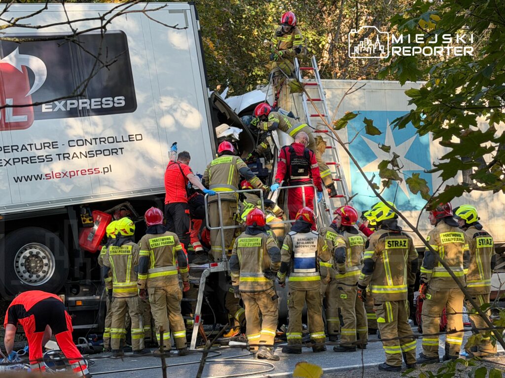 Strażacy wchodzą po drabinach do naczepy ciężarówki podczas akcji ratunkowej przy drodze