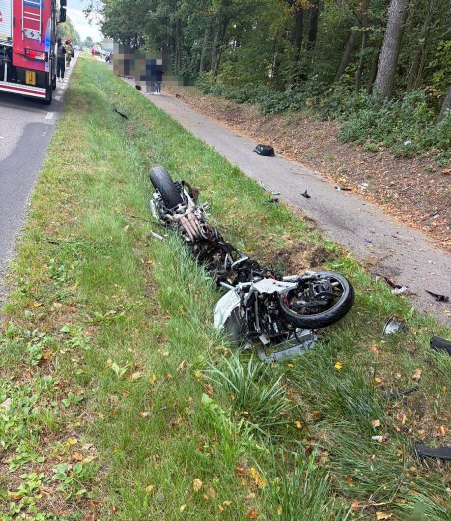 Zniszczony motocykl leży na trawie przy drodze, obok strażacy oraz osoby udzielające pomocy.