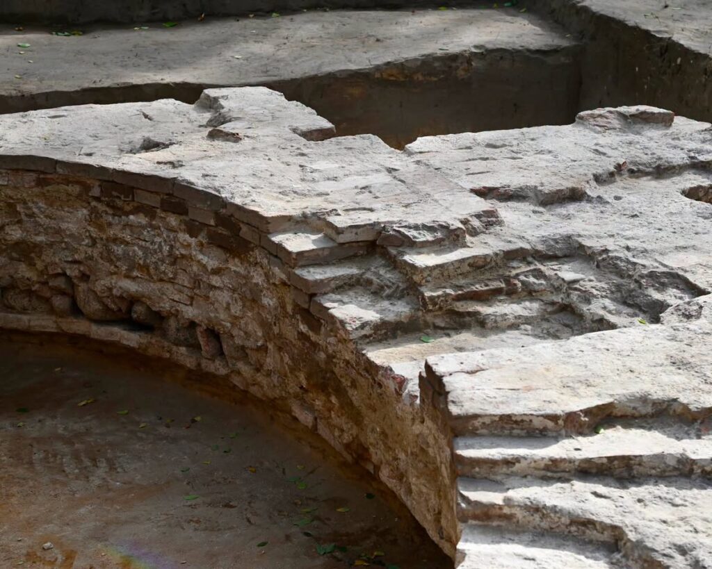 Zabytkowe fragmenty murów z widocznymi warstwami kamieni w wykopie archeologicznym.
