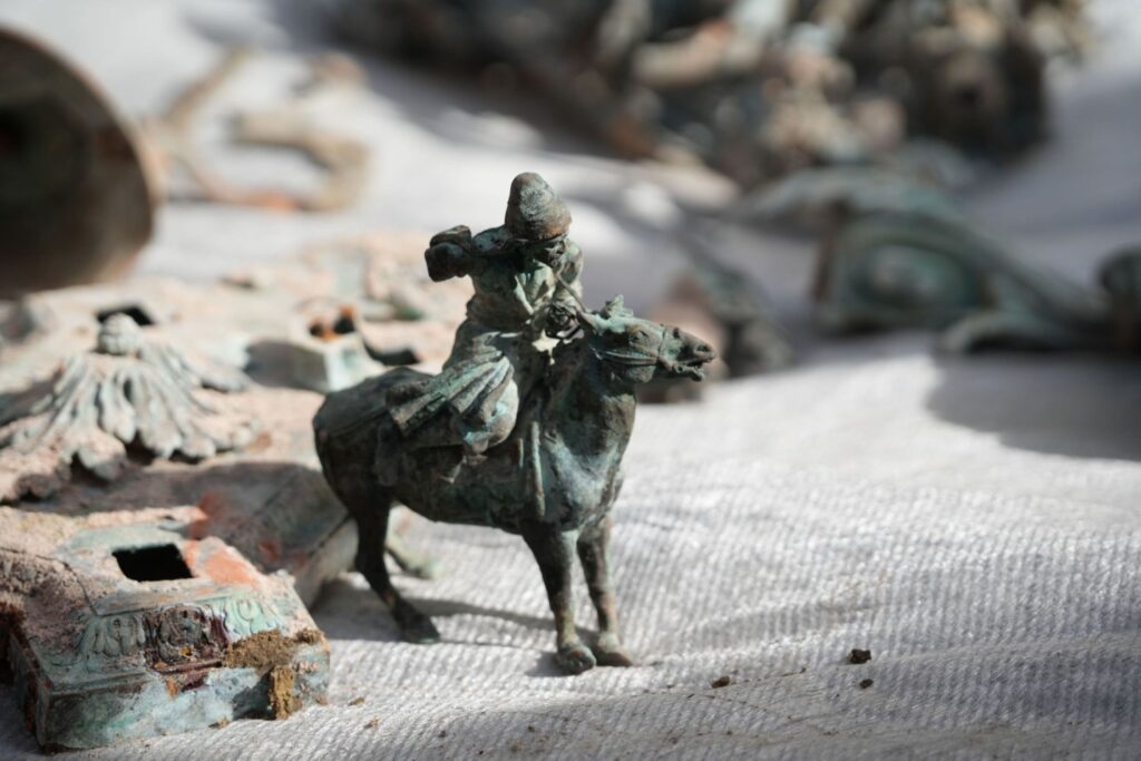Figurka jeźdźca na koniu wykonana z brązu, otoczona innymi artefaktami na białym tle.