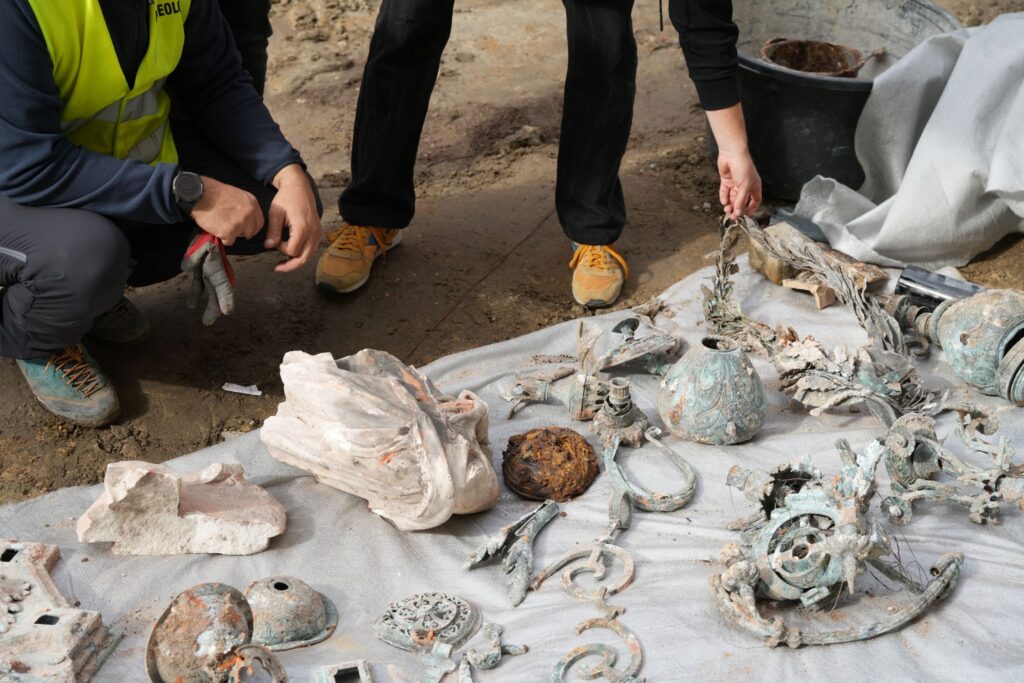 Archeolodzy przeglądają odkryte artefakty na białym płótnie w terenie wykopaliskowym.