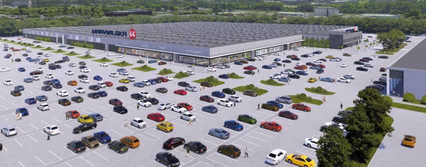 Nowoczesne centrum handlowe Marywilska 44 z dużym parkingiem, na którym zaparkowane są różnokolorowe samochody.