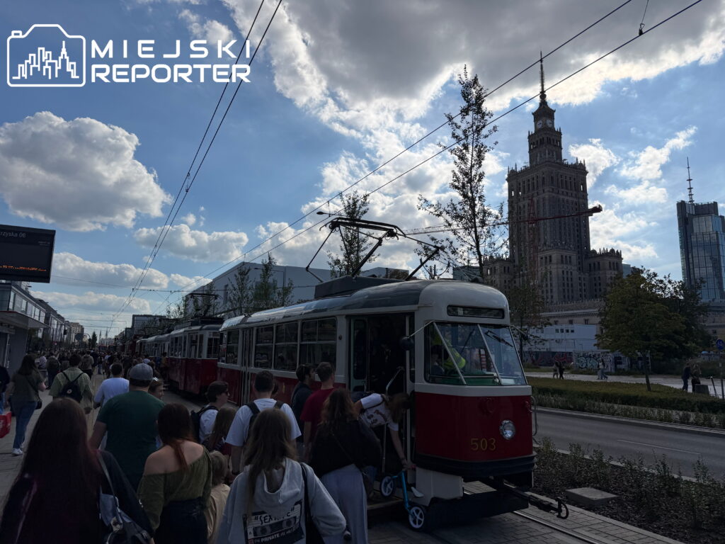 Tłum ludzi obserwujących tramwaje podczas Mistrzostw motorniczych na ulicy z widokiem na wieżowiec.