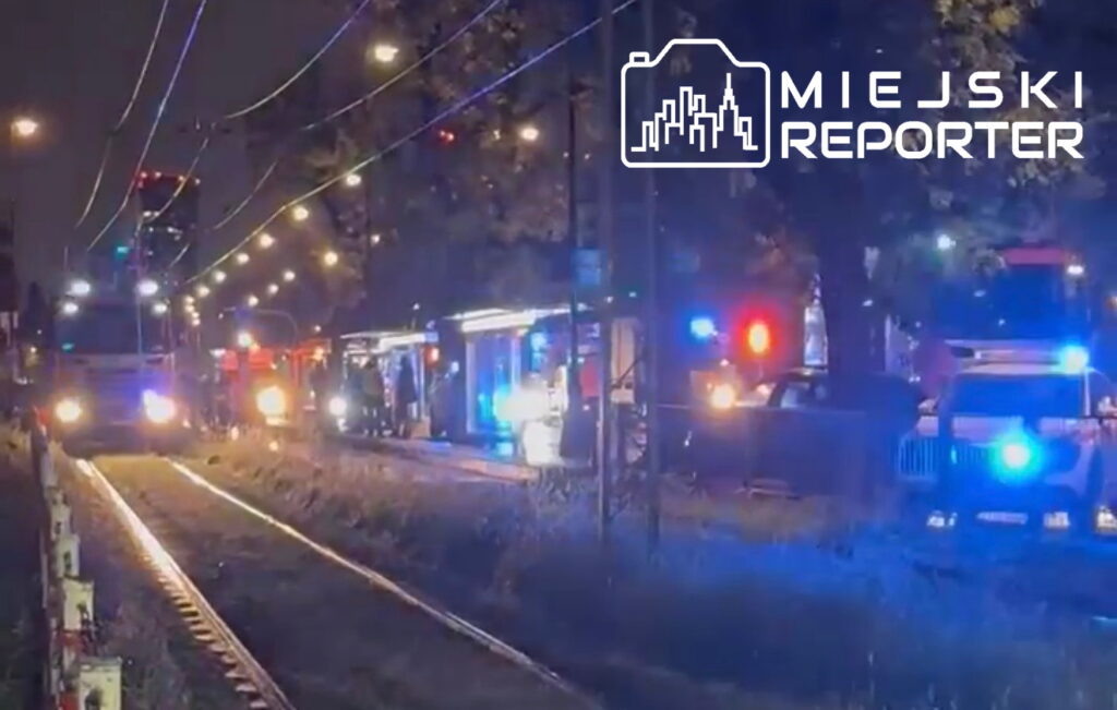 Służby ratunkowe z włączonymi sygnałami świetlnymi zatrzymane wzdłuż torów tramwajowych w nocnym otoczeniu.