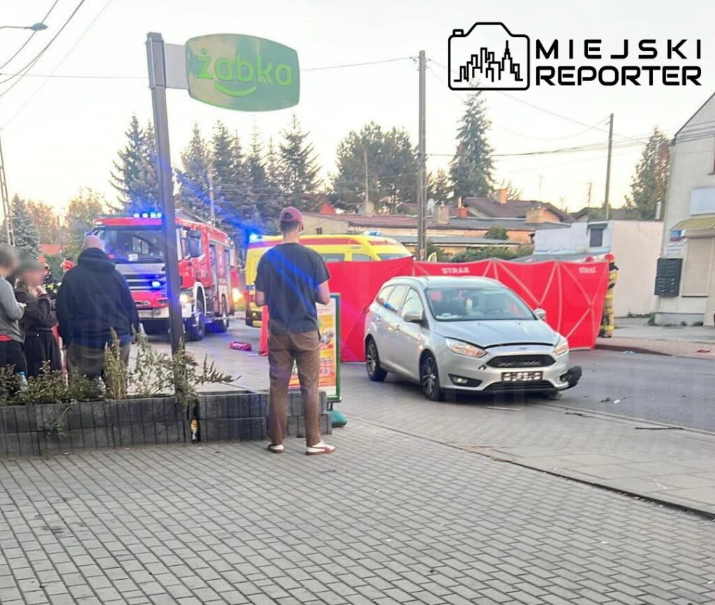 Kierowca samochodu osobowego stoi obok uszkodzonego pojazdu na chodniku, obok akcji ratunkowej w Arkuszowej. W tle widać straż pożarną.