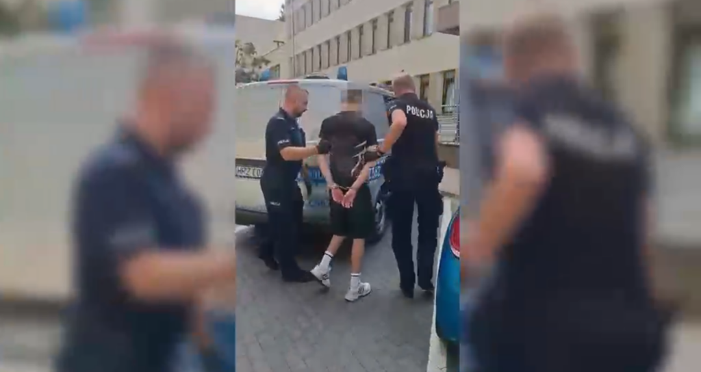 Młody mężczyzna w rękach policji, zatrzymywany w pobliżu radiowozu na ulicy, po podejrzeniu o rozbój.