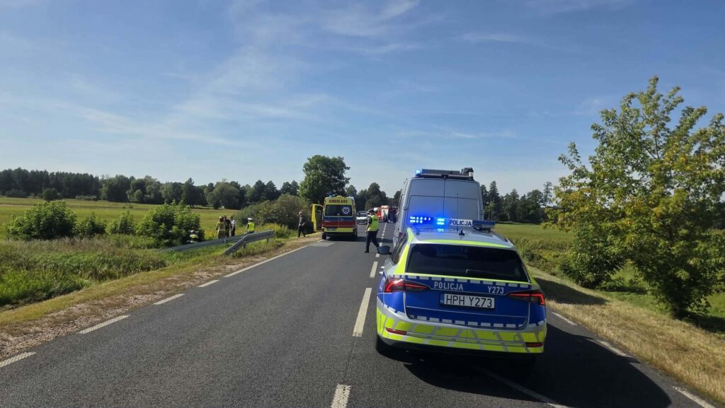 Na drodze zatrzymane pojazdy ratunkowe, w tym radiowóz policyjny i karetka, obok grupka osób w odzieży roboczej.
