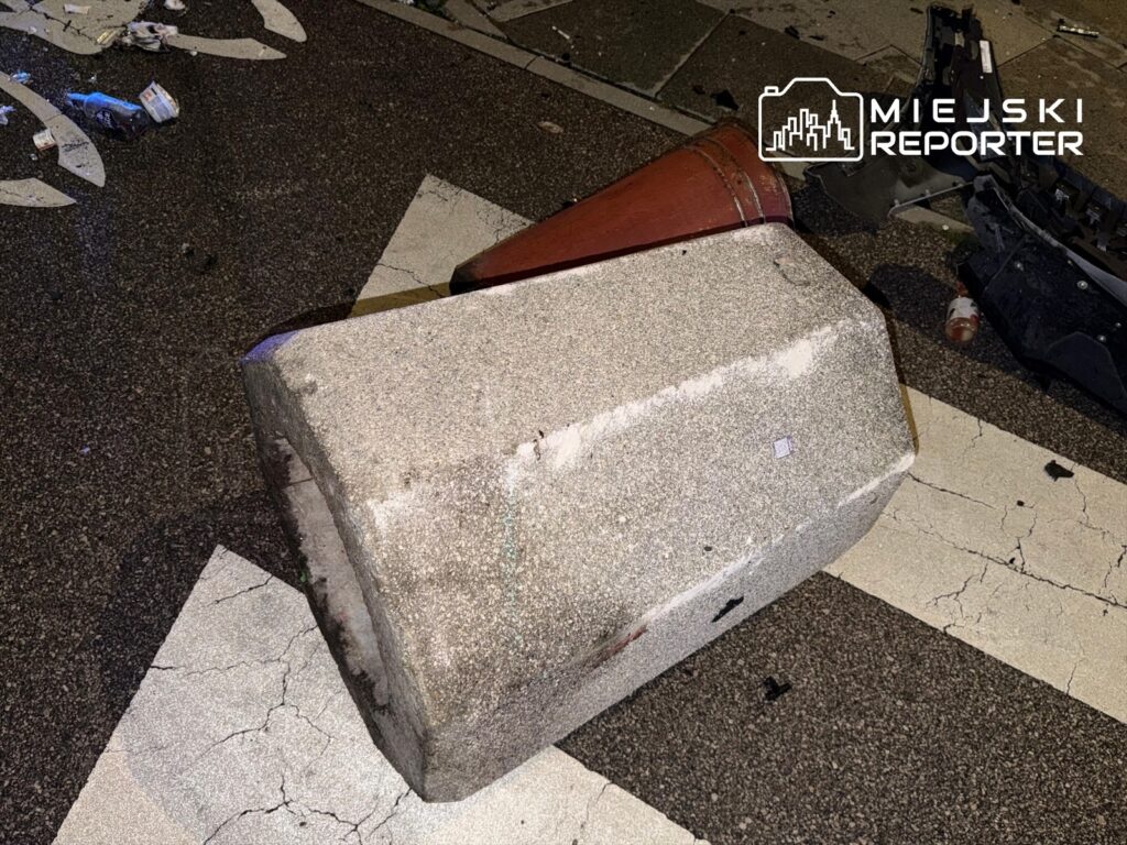 Zniszczony betonowy słupek leży na jezdni, obok widać porozrzucane śmieci i uszkodzone elementy drogi.