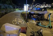 BMW z uszkodzonym przodem stoi na chodniku, obok przewrócony kosz na śmieci oraz rozbite elementy otoczenia.