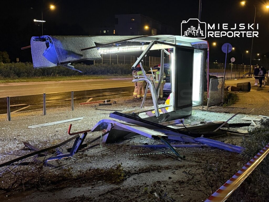 Zniszczony przystanek autobusowy z rozbitym dachem i porozrzucanymi elementami, w tle widać interwencję służb ratunkowych.