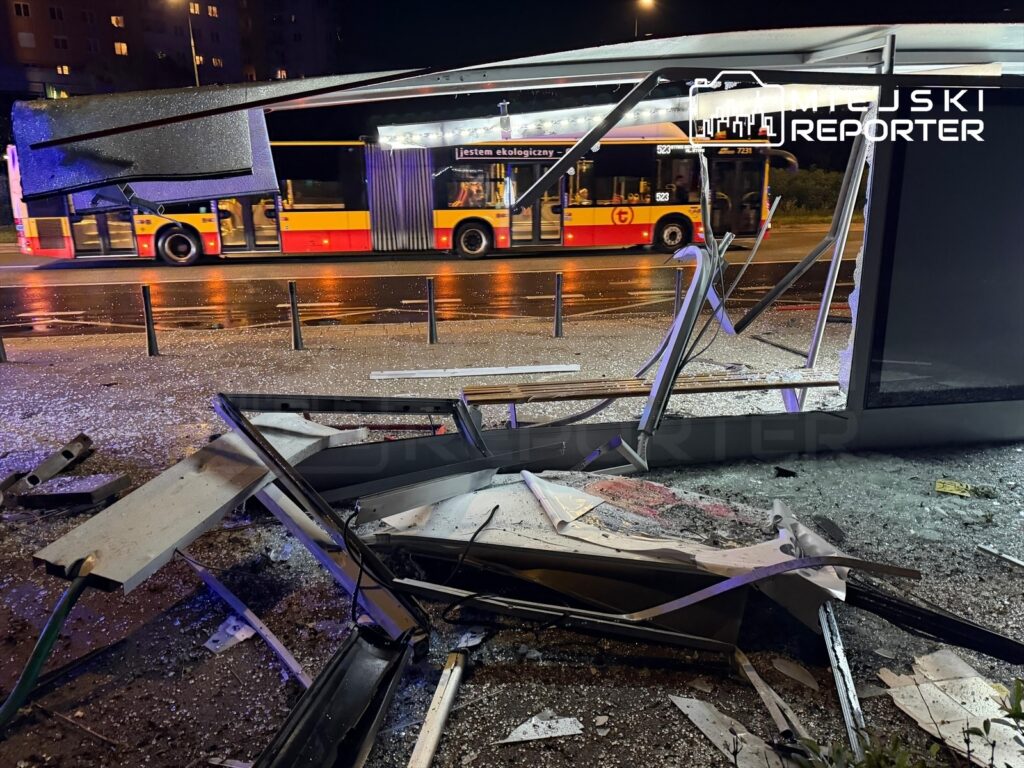 Zniszczony przystanek autobusowy z połamanymi elementami konstrukcyjnymi i rozbitym szkłem, obok przejeżdżający autobus.