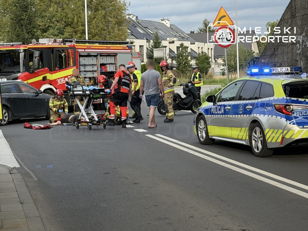 Ratownicy medyczni udzielają pomocy motocykliście leżącemu na jezdni, obok stoi policyjny radiowóz.