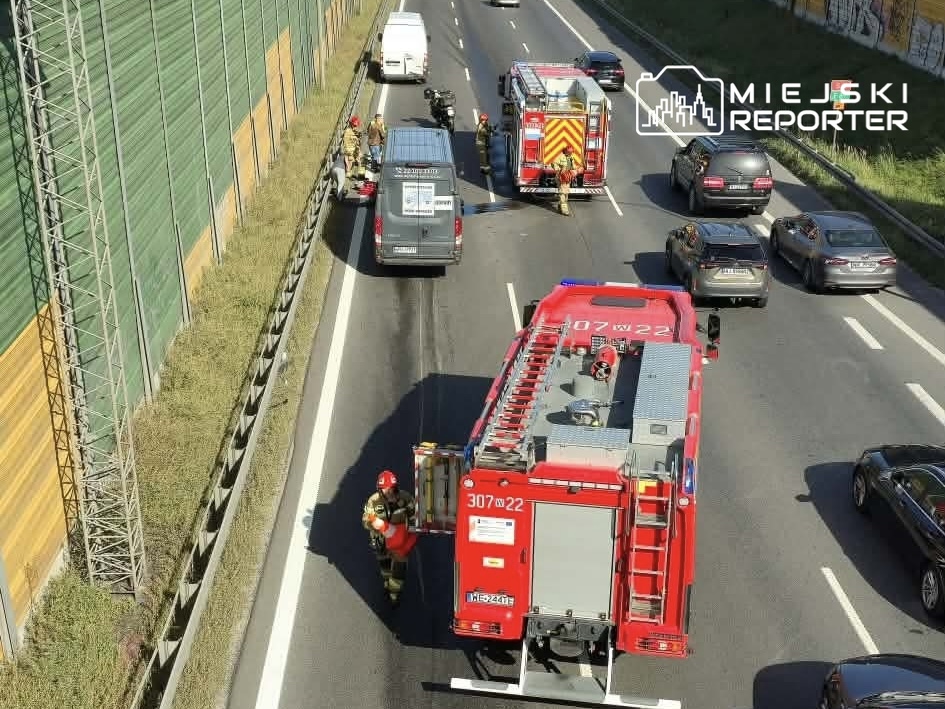 Strażacy przy pomocy sprzętu ratunkowego pracują na jezdni, obok wozu strażackiego, w miejscu wypadku drogowym.