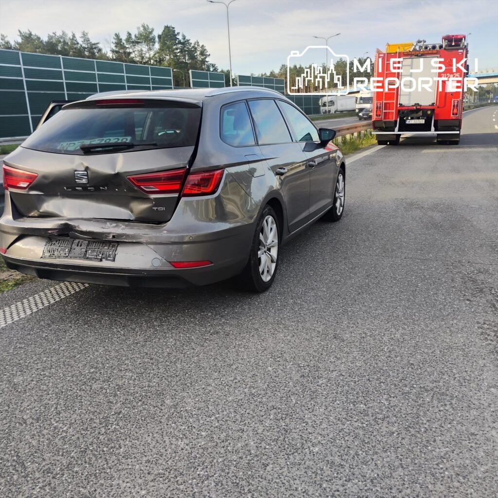 Zniszczony samochód osobowy zaparkowany na poboczu drogi, obok widać wóz strażacki.