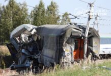 Zderzony pociąg z uszkodzoną kabiną maszynisty leży na torach w otoczeniu zieleni i drzew.