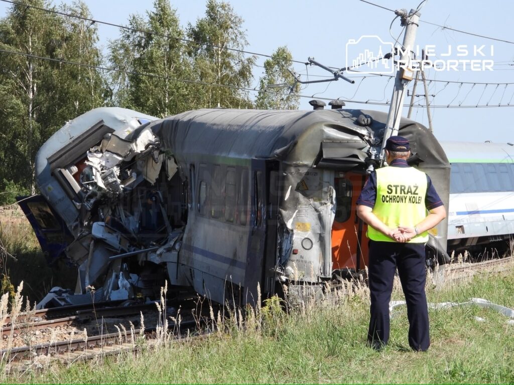 Zniszczony wagon kolejowy po wypadku, obok stoi funkcjonariusz straży ochrony kolei, obserwując sytuację.
