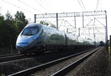 Pociąg Pendolino poruszający się po torach w otoczeniu zieleni, z widocznymi słupami trakcyjnymi w tle.