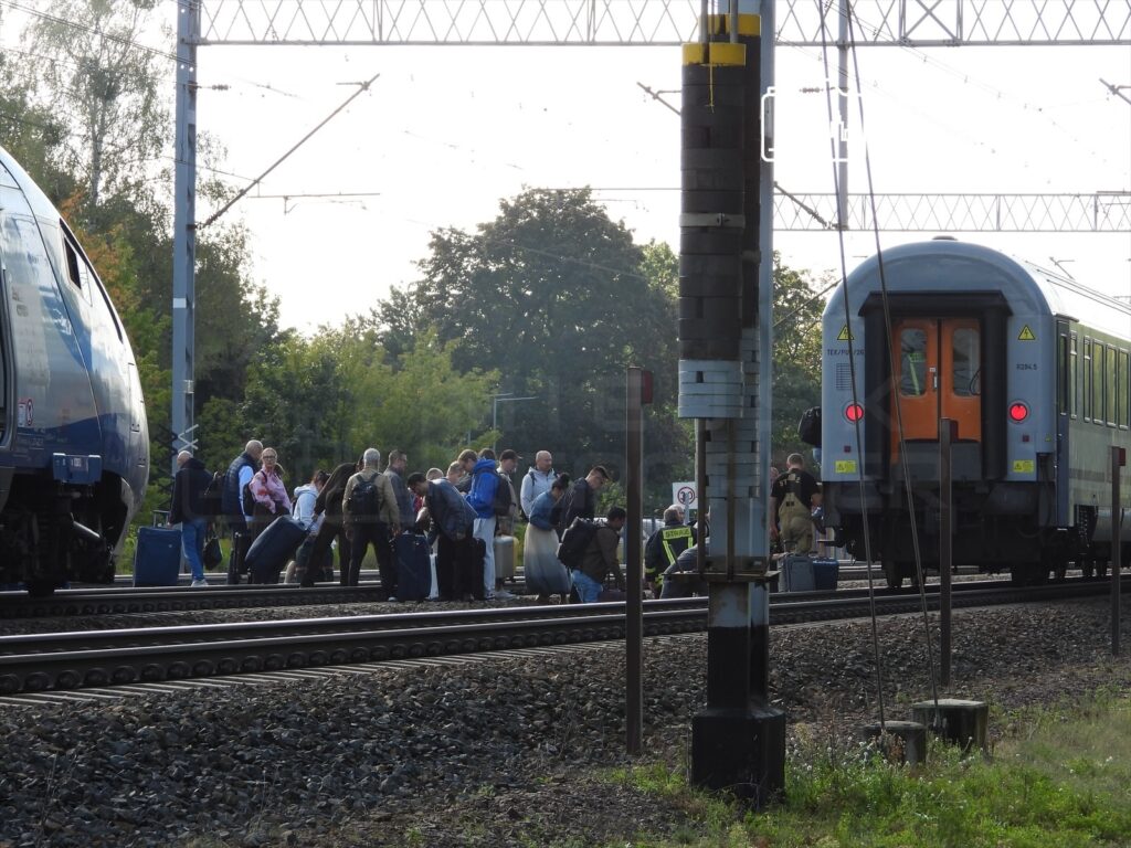 Pasażerowie z bagażami gromadzą się na torach kolejowych, czekając na ewakuację po wypadku z udziałem mężczyzny.