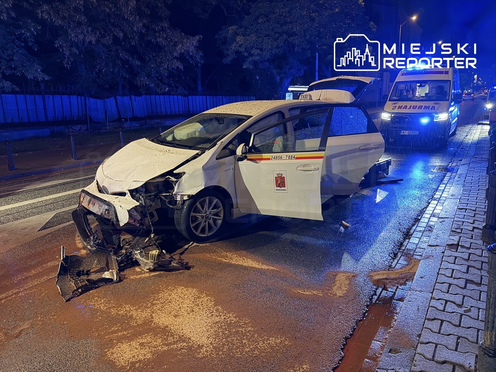 Uszkodzony samochód osobowy z oderwaną przednią częścią stoi na ulicy, obok widać ambulans.
