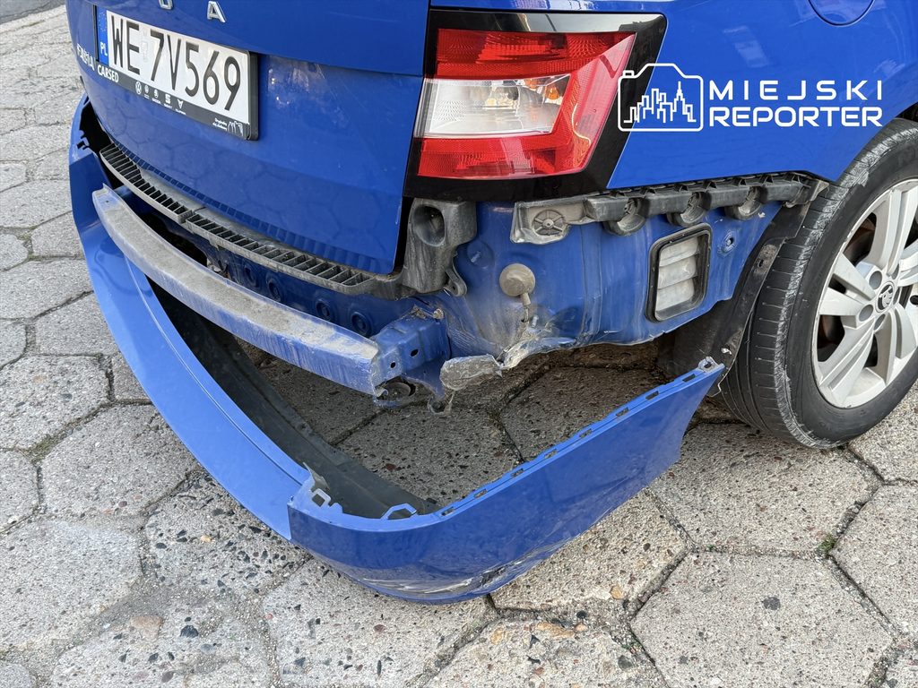 Uszkodzony tył niebieskiej Skody z odczepionym zderzakiem, stojącej na kostce brukowej.