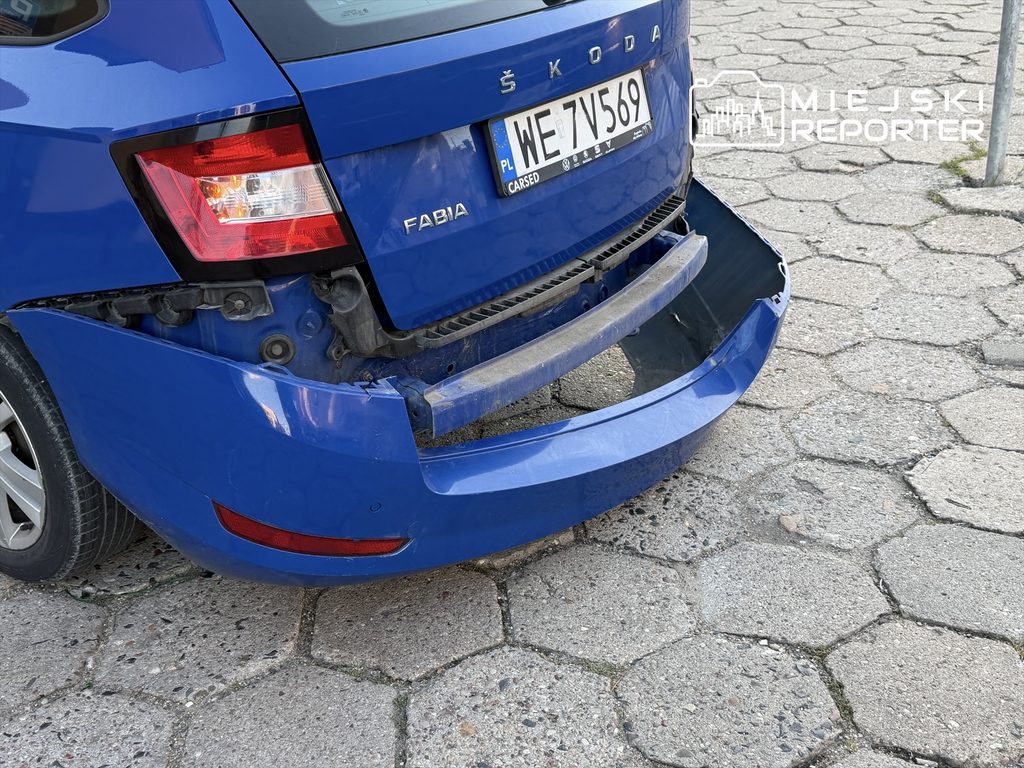 Uszkodzona tylna część niebieskiej Skody Fabii z oderwanym zderzakiem, stojącej na kostce brukowej.
