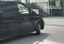 Czarny samochód z logo "FUNERAL ZAKŁAD POGRZEBOWY" zaparkowany przy nowoczesnym budynku.
