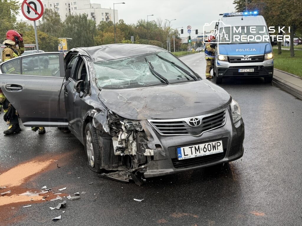 Zniszczony samochód osobowy marki Toyota z uszkodzoną przednią częścią stoi na jezdni, obok pracują strażacy.